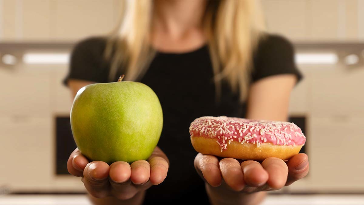 Women holding an apple in one hand and a donut in the other